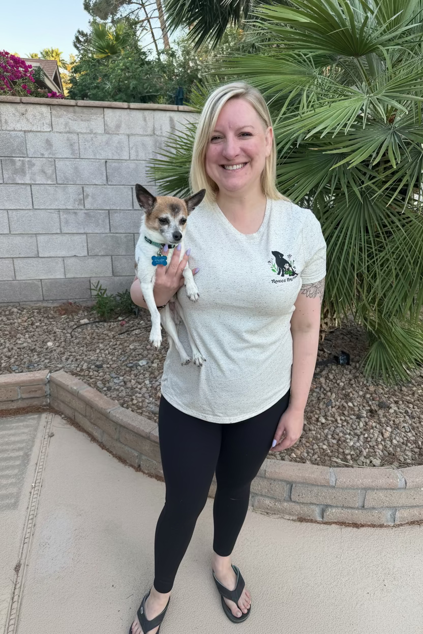 Woman holding a small dog outdoors with plants and a wall in the background